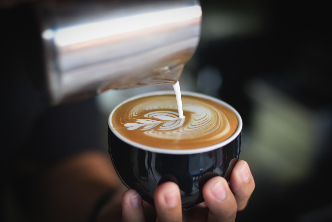 A hand is holding a coffee cup which has milk being poured into it.